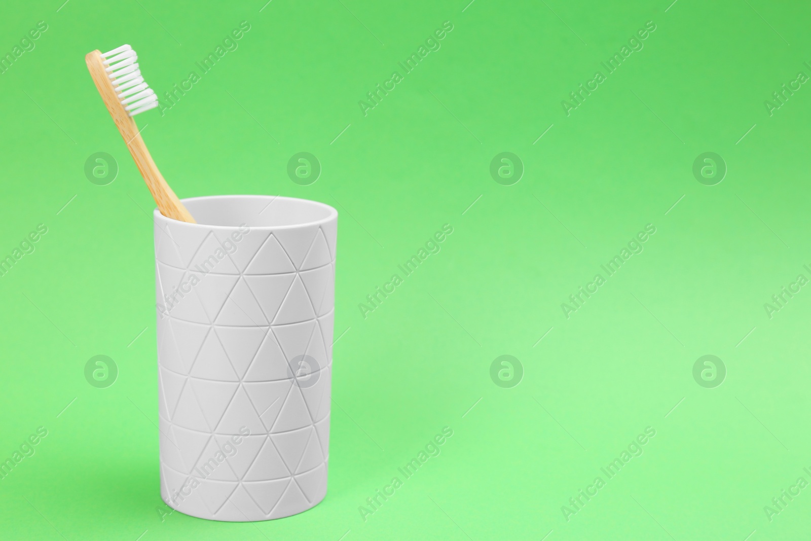 Photo of Bamboo toothbrush in holder on green background, space for text