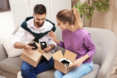 Photo of Young couple opening parcels on sofa in living room