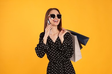 Photo of Happy young woman with shopping bags and smartphone on yellow background. Big sale