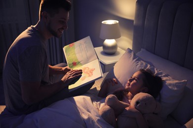 Photo of Father reading bedtime story to his daughter at home