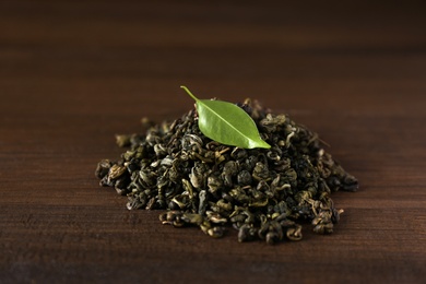 Photo of Heap of dried green tea leaves on wooden table