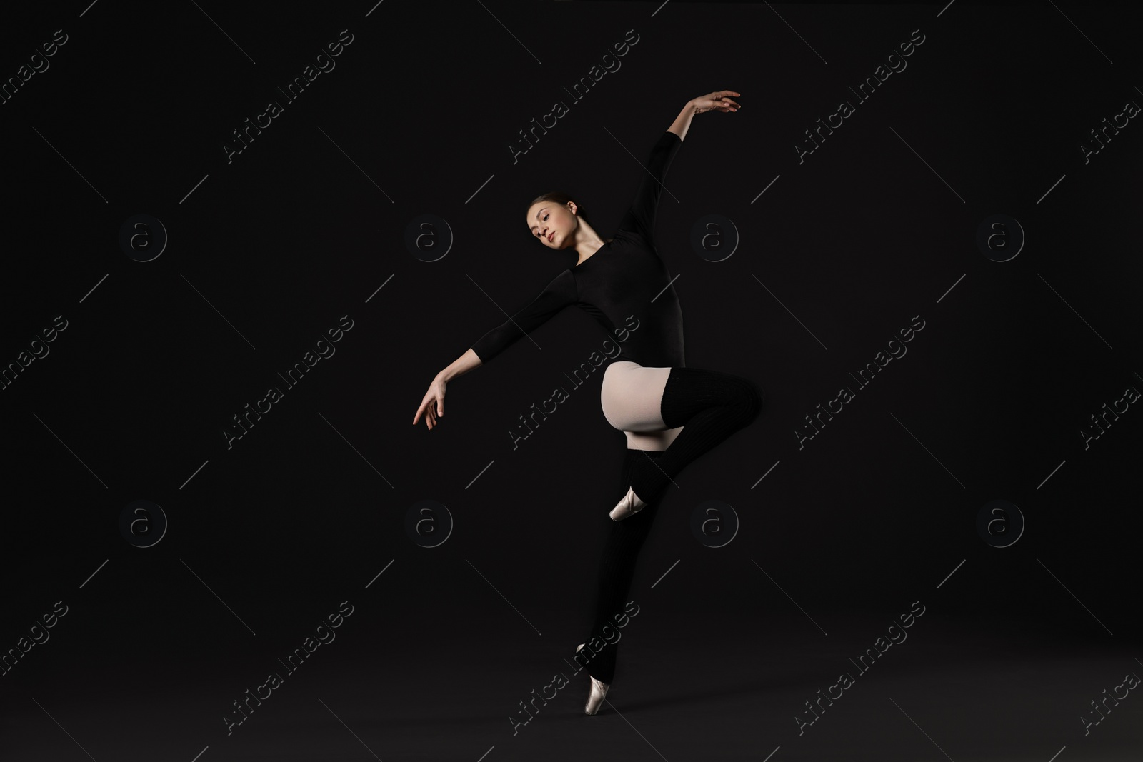 Photo of Young ballerina practicing dance moves on black background