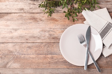 Beautiful table setting with cutlery, napkin and plate on wooden background, top view. Space for text