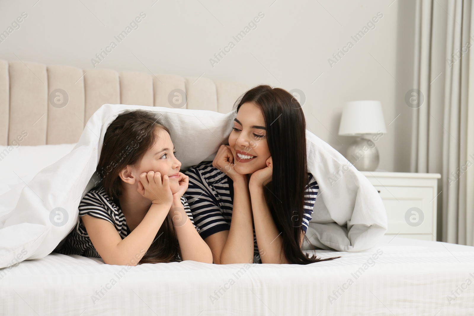 Photo of Young mother and her daughter under blanket in bed at home