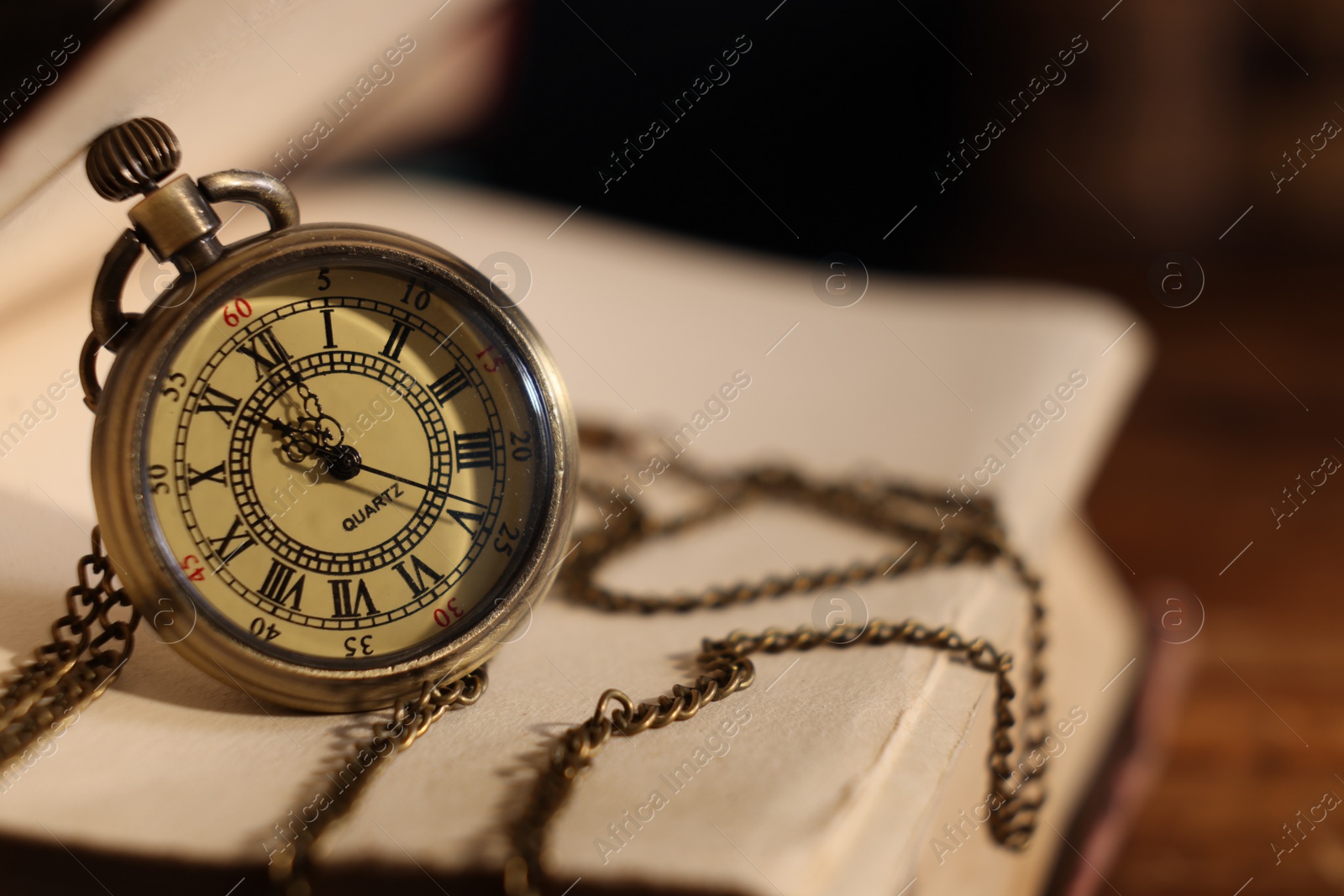 Photo of Pocket clock with chain and book on table, closeup. Space for text
