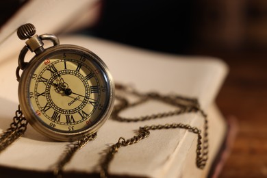 Pocket clock with chain and book on table, closeup. Space for text