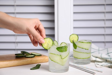 Photo of Woman decorating glass of tasty fresh cucumber water at white table, closeup