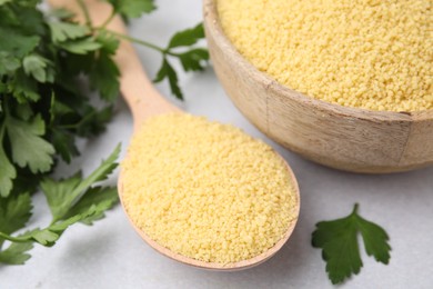 Photo of Raw couscous in bowl, spoon and parsley on light table, closeup