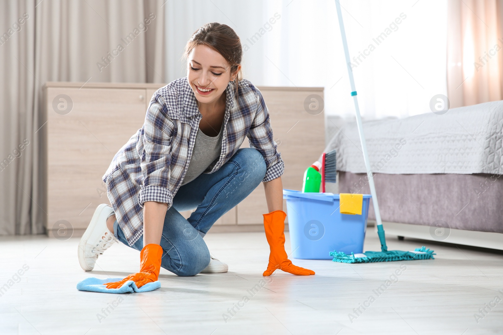 Photo of Young woman washing floor with rag and detergent in bedroom. Cleaning service