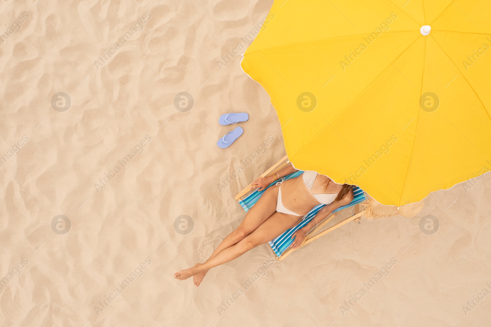 Image of Woman resting in sunbed under yellow beach umbrella at sandy coast, aerial view. Space for text