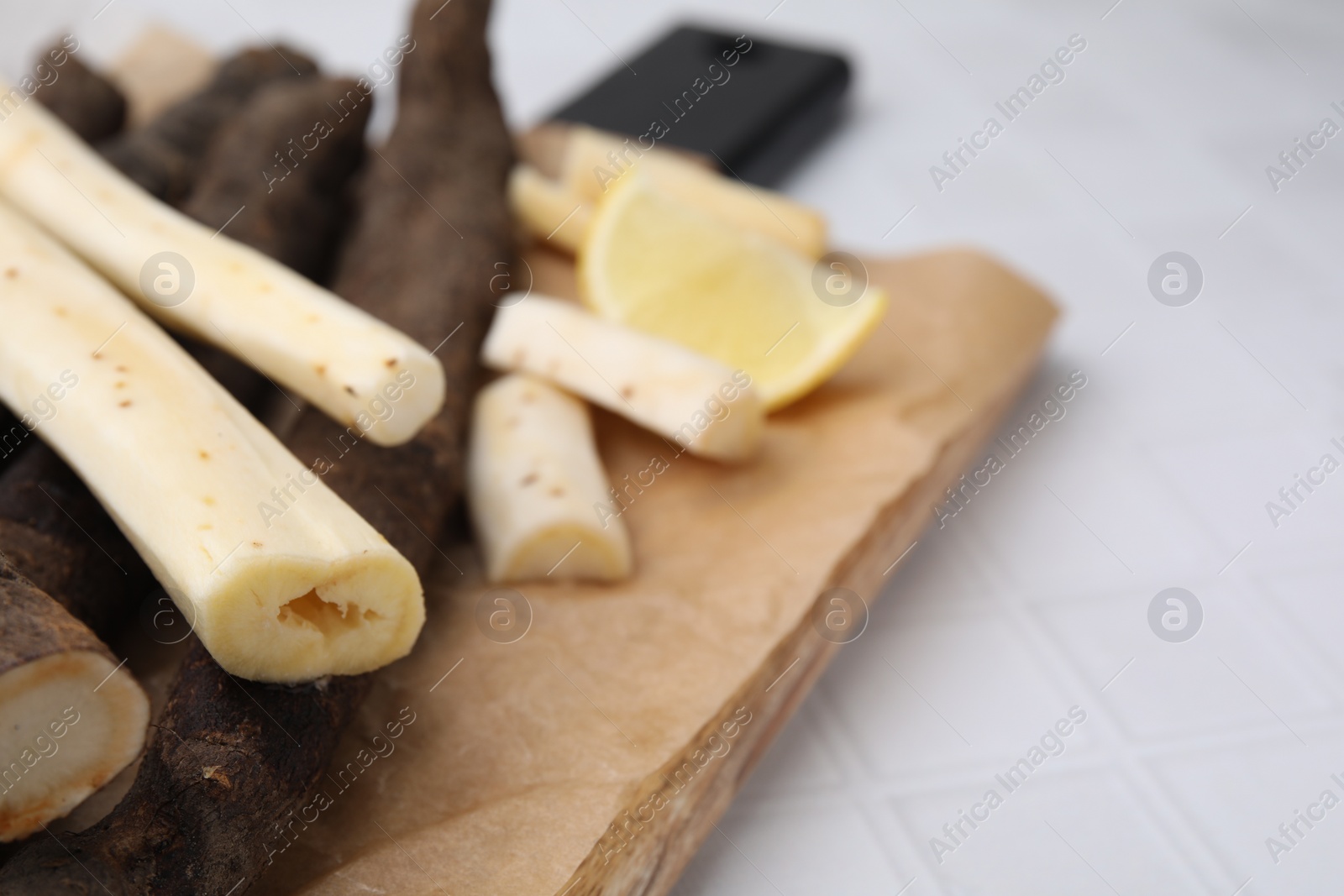 Photo of Raw salsify roots and lemon on white tiled table, closeup. Space for text