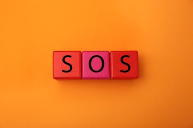 Photo of Abbreviation SOS (Save Our Souls) made of color cubes with letters on orange background, top view