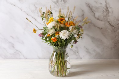 Photo of Bouquet of beautiful wild flowers and spikelets in vase on white wooden table against marble background