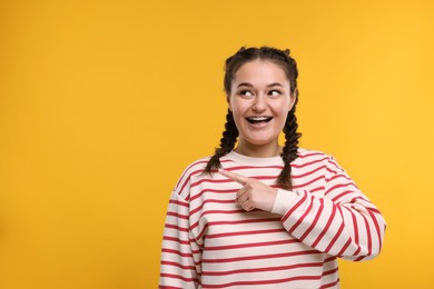 Happy woman with braces pointing at something on orange background. Space for text