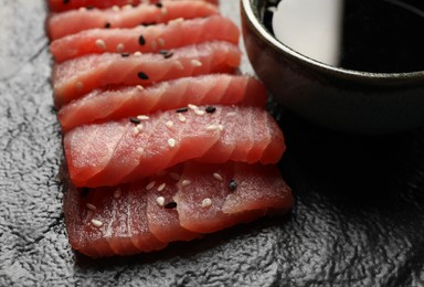 Tasty sashimi (pieces of fresh raw tuna with sesame seeds) on black plate, closeup