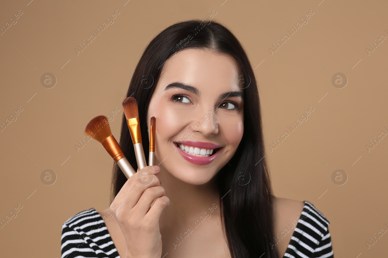 Photo of Happy woman with different makeup brushes on light brown background