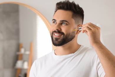 Handsome man applying cosmetic serum onto his face in bathroom