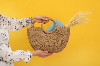 Photo of Woman holding beach bag with beautiful bouquet of wildflowers and book on yellow background, closeup