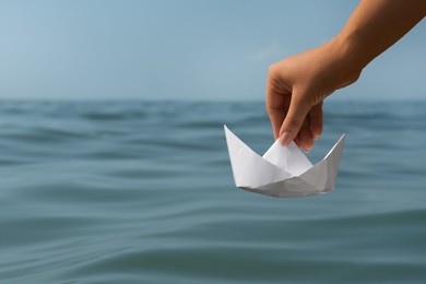 Photo of Woman holding white paper boat near sea, closeup. Space for text
