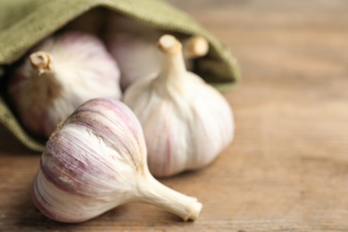Photo of Fresh unpeeled garlic bulbs on wooden table, closeup with space for text. Organic product