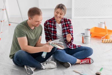 Photo of Happy couple with paint chips discussing new wall color in apartment during repair
