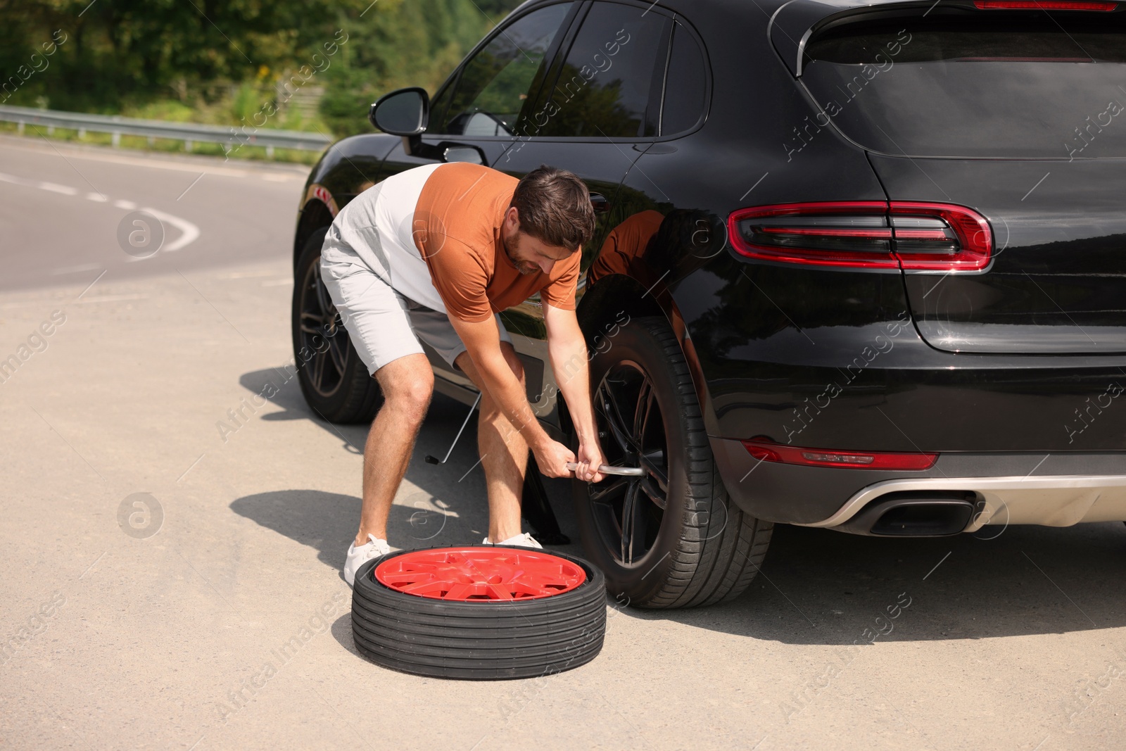 Photo of Man changing wheel of car on roadside outdoors