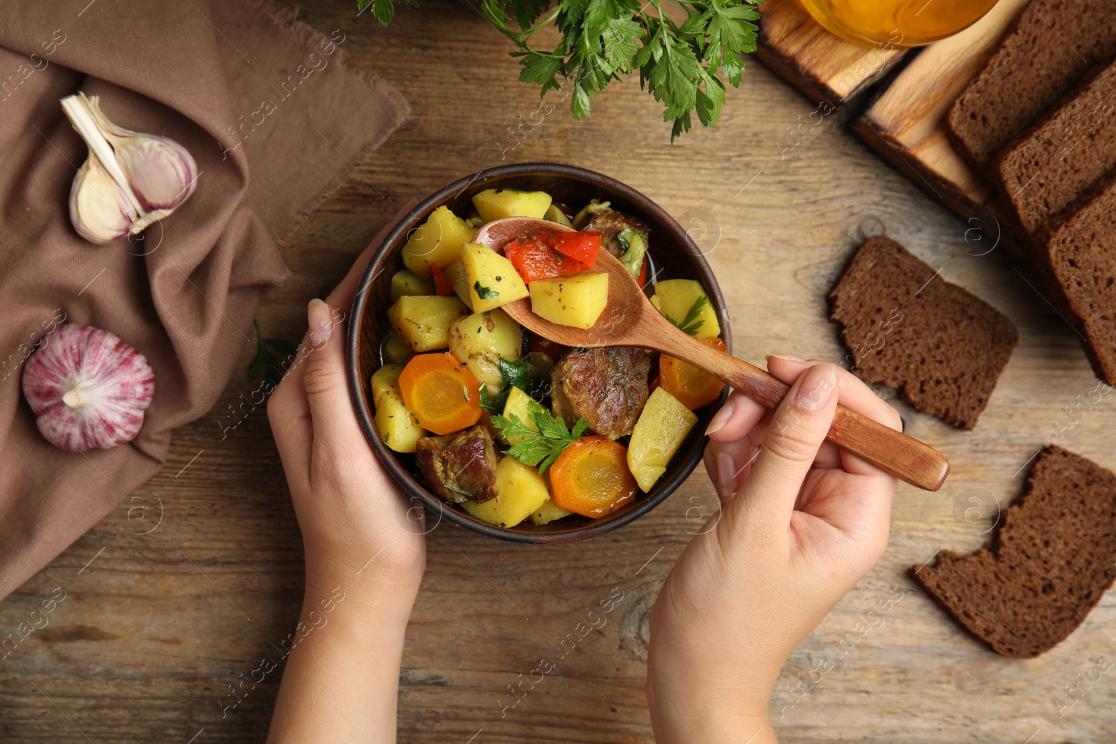 Photo of Woman eating delicious dish with potatoes from earthenware at wooden table, top view