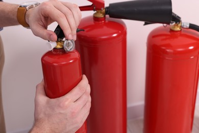 Photo of Man checking quality of fire extinguishers indoors, closeup