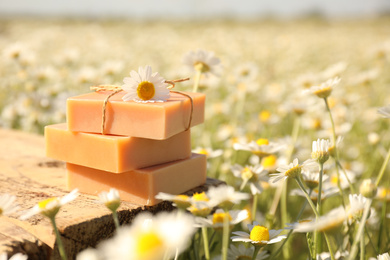Photo of Bars of soap on wooden table in chamomile field