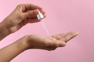 Photo of Woman applying cosmetic serum onto her hand on pink background, closeup