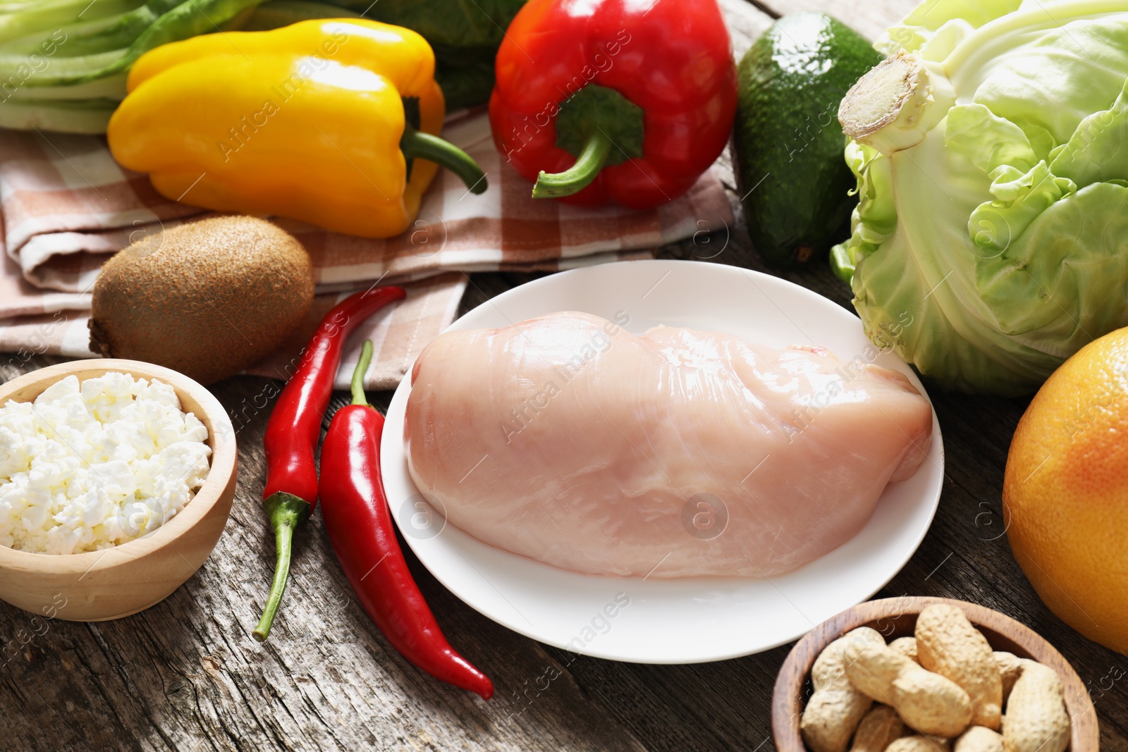 Photo of Healthy meal. Different vegetables and raw chicken breast on wooden table, closeup