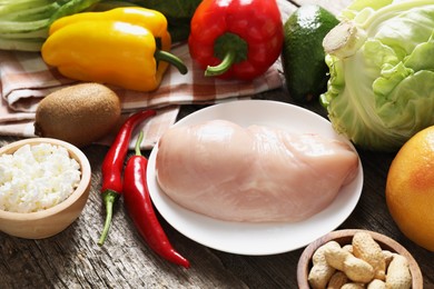 Photo of Healthy meal. Different vegetables and raw chicken breast on wooden table, closeup