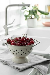 Photo of Fresh ripe cherries with water drops in colander on countertop indoors