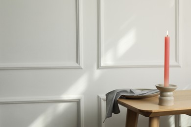 Photo of Holder with burning candle on wooden table near white wall indoors