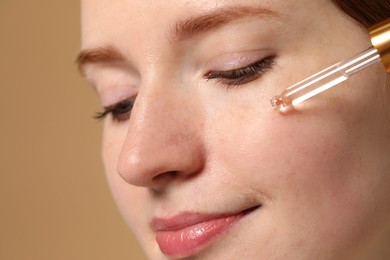 Photo of Beautiful woman with freckles applying cosmetic serum onto her face on beige background, closeup