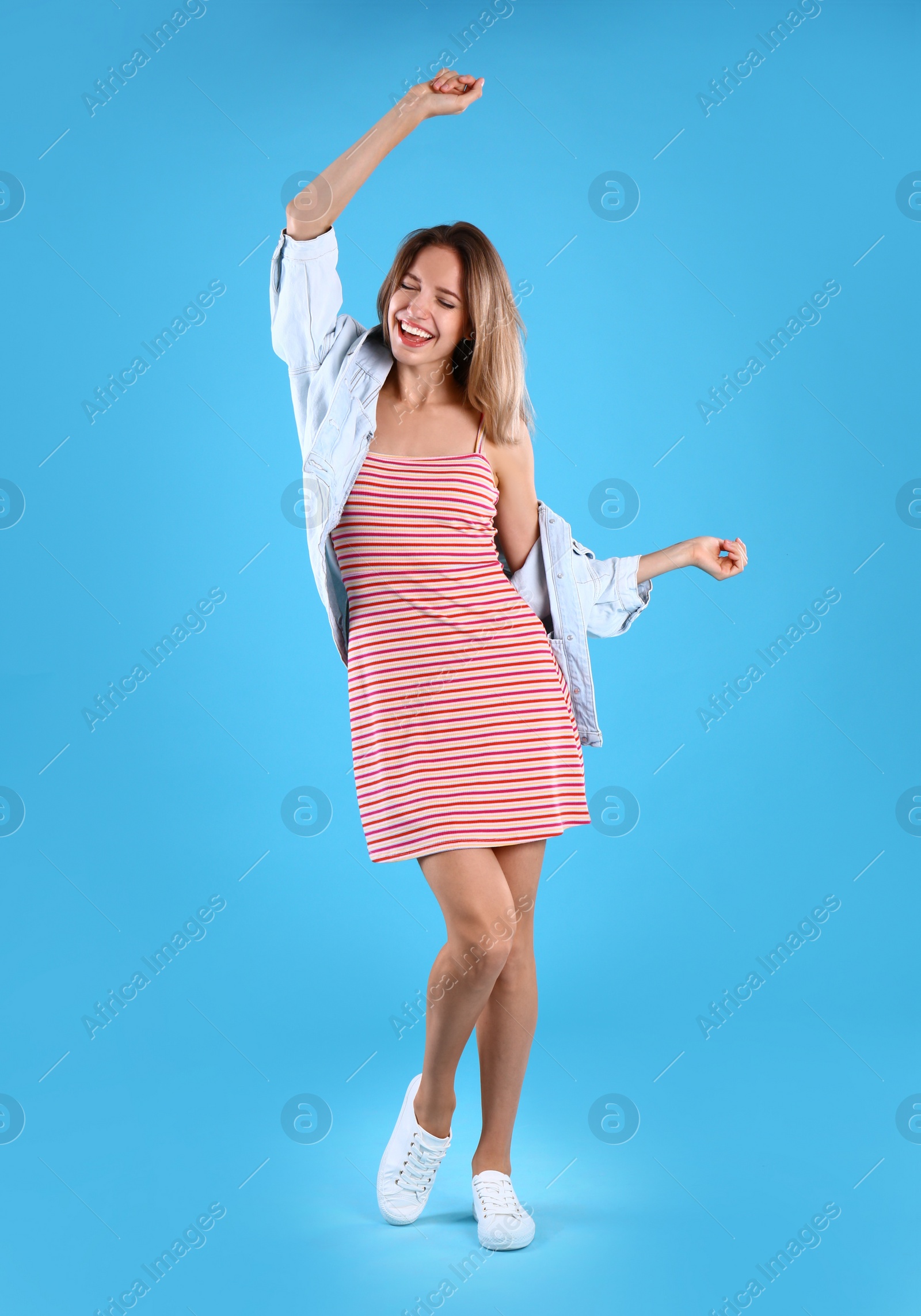 Photo of Beautiful young woman in dress and jacket dancing on blue background