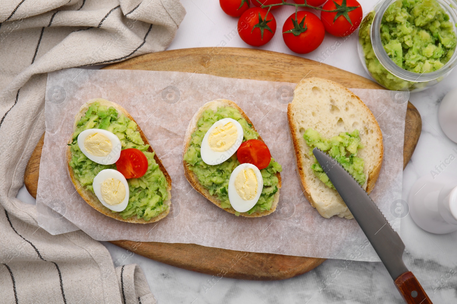 Photo of Delicious sandwiches with guacamole, eggs and tomatoes on white table, flat lay