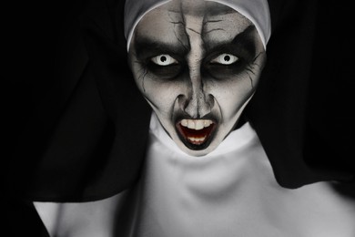 Photo of Portrait of scary devilish nun on black background, closeup. Halloween party look