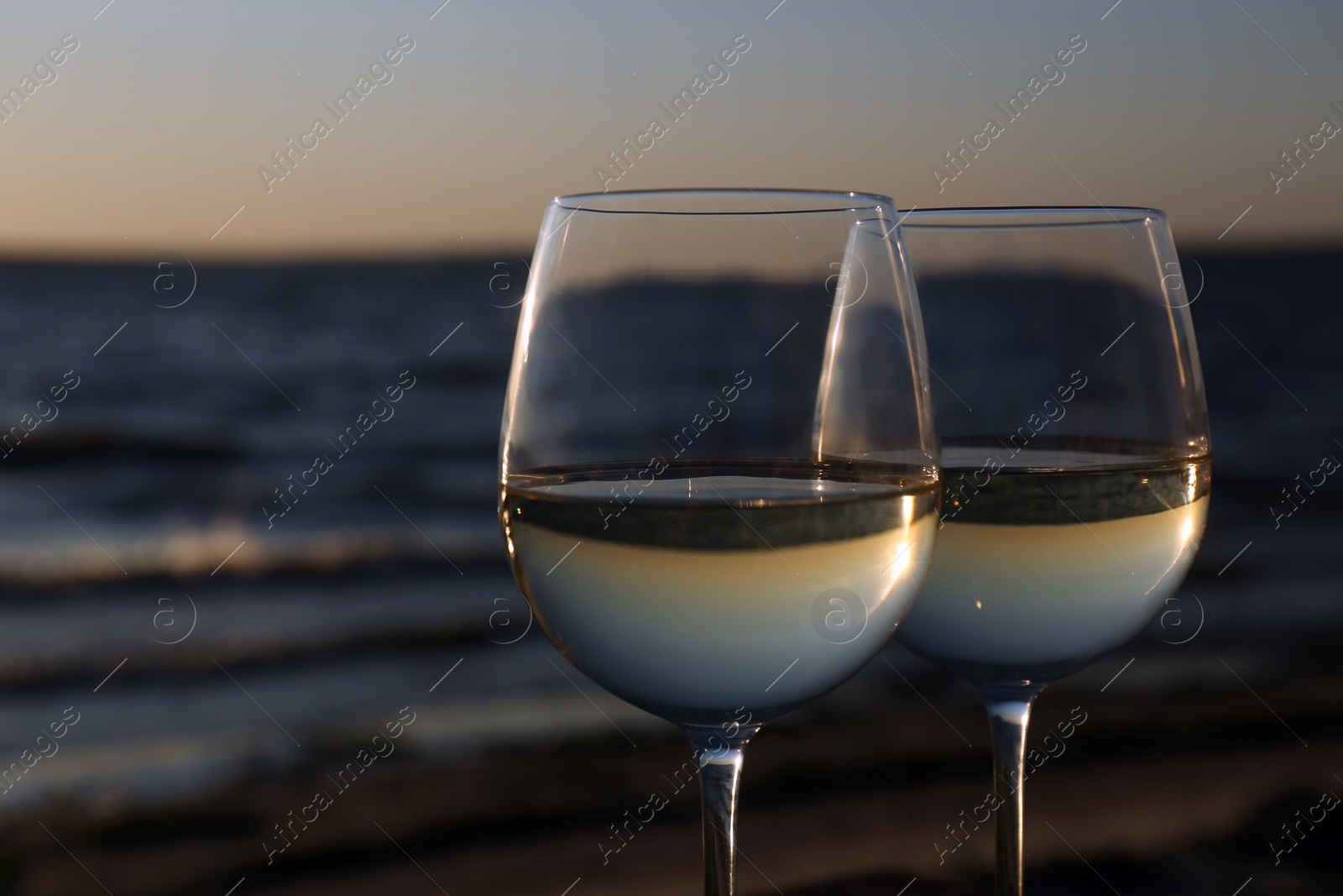 Photo of Two glasses of wine near river at sunset, closeup. Space for text