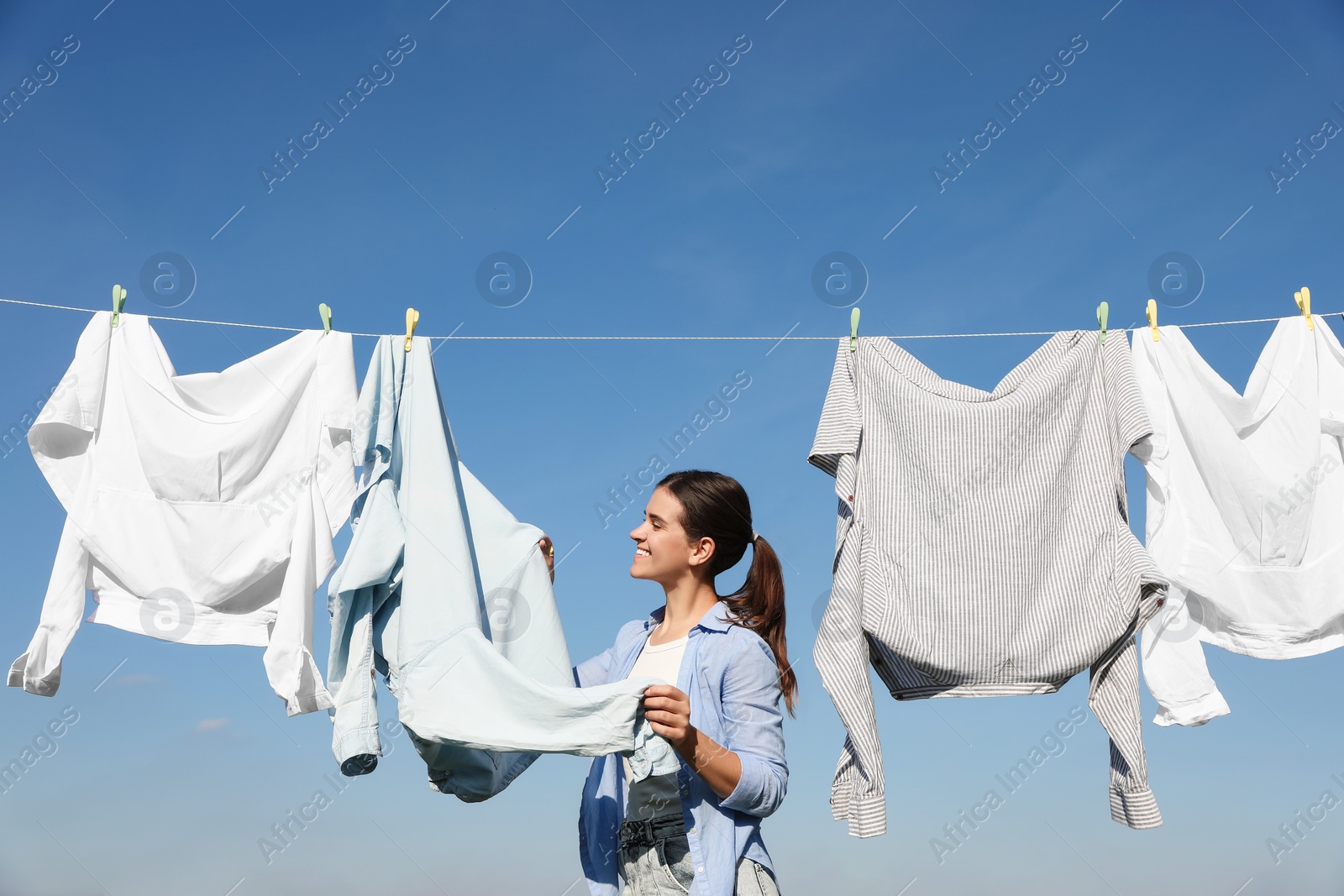 Photo of Woman hanging clothes with clothespins on washing line for drying against blue sky