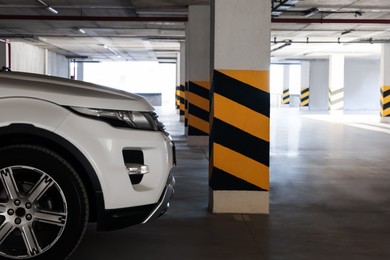 Photo of White car near column with warning stripes in parking garage