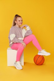 Photo of Cute indie girl with basketball ball on yellow background