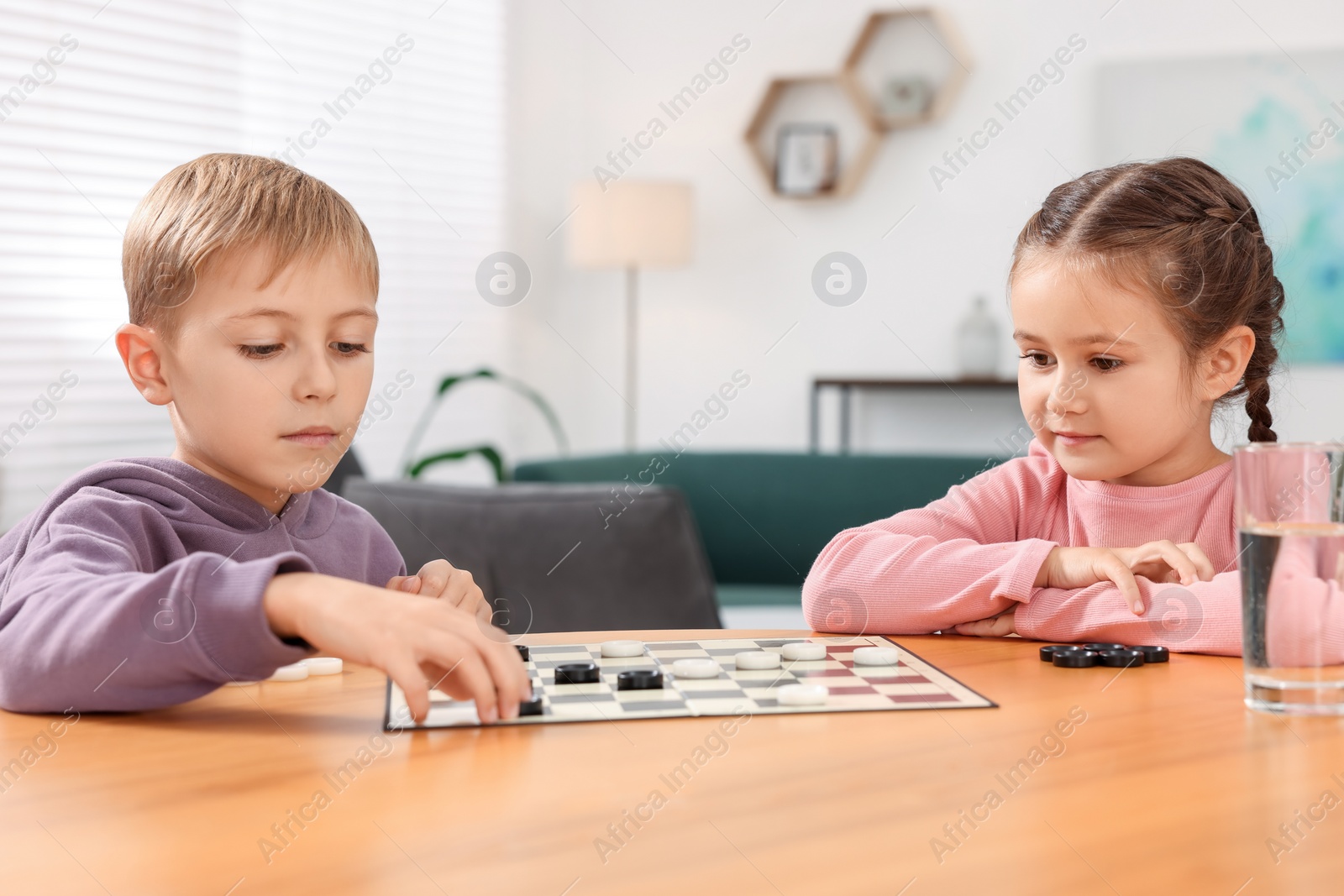 Photo of Cute children playing checkers at wooden table in room