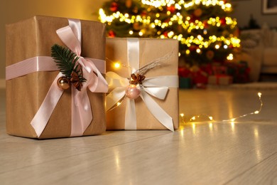 Beautiful gift boxes against fir tree with Christmas lights indoors, space for text
