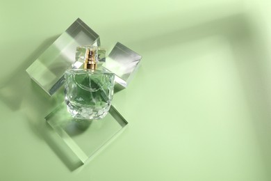 Stylish presentation of luxury perfume in sunlight on olive background, flat lay. Space for text