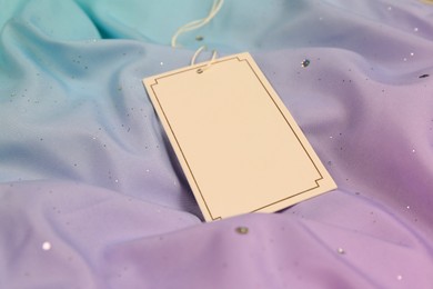 Photo of Blank white tag on color fabric. Space for text