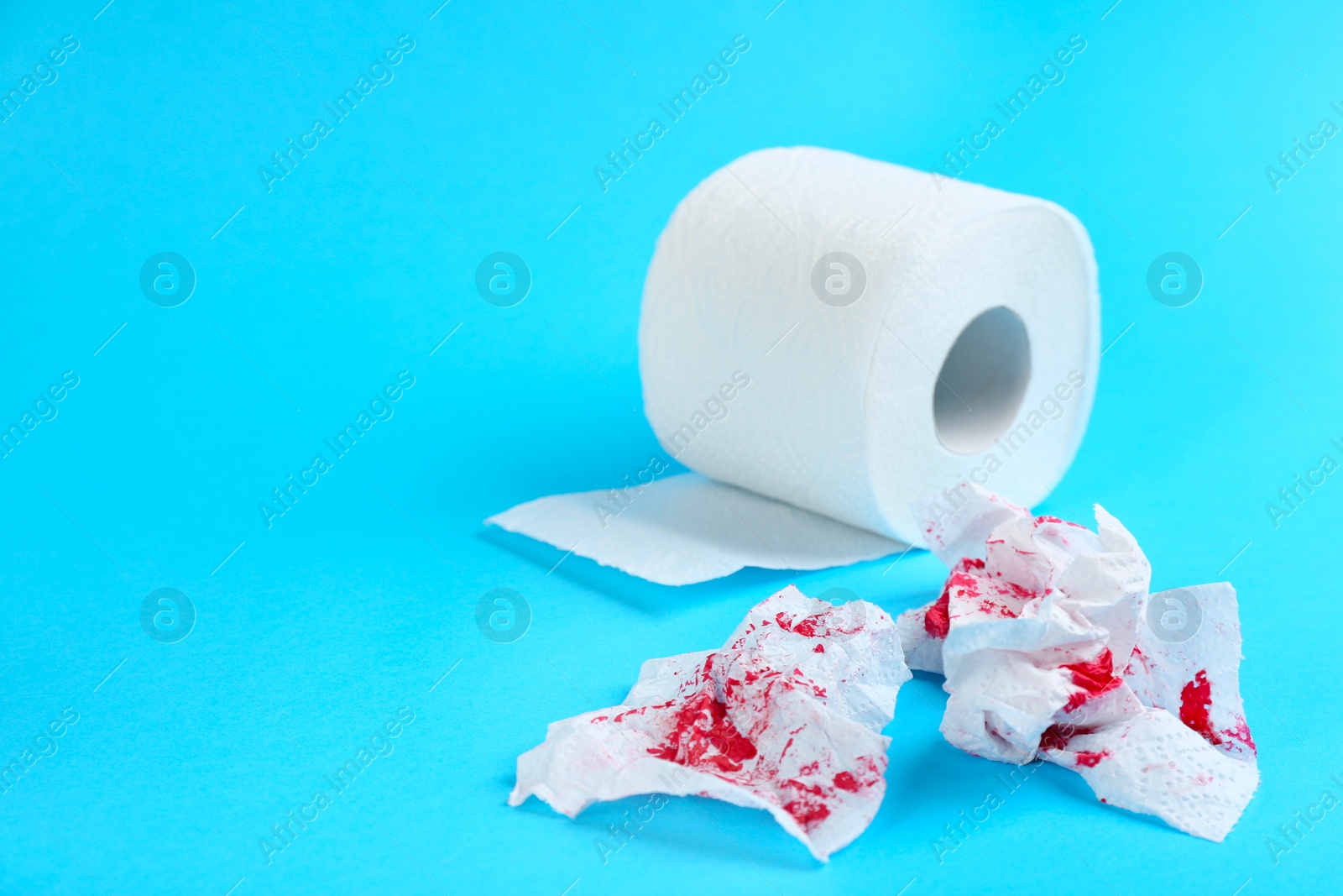 Photo of Sheets of toilet paper with blood on light blue background, space for text. Hemorrhoid problems