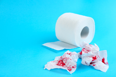 Photo of Sheets of toilet paper with blood on light blue background, space for text. Hemorrhoid problems