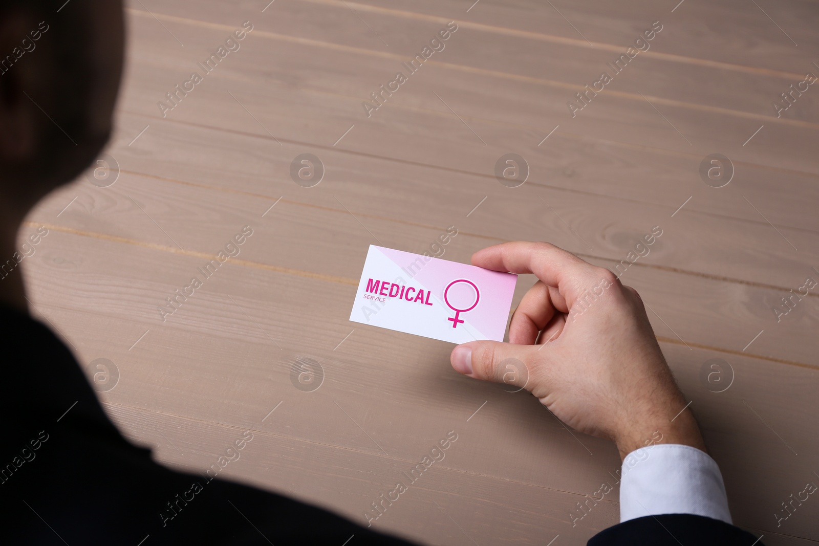 Photo of Man holding medical business card at wooden table, closeup. Women's health service