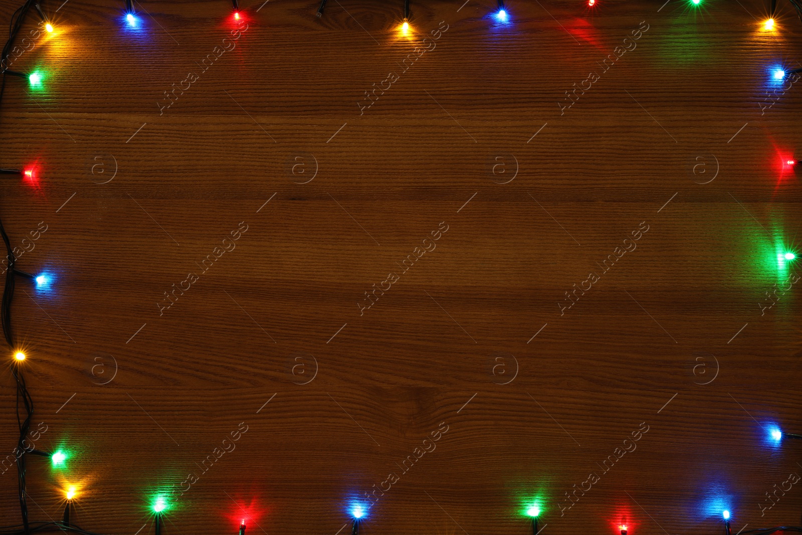 Photo of Frame of colorful Christmas lights on wooden table, top view. Space for text